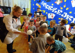 Dzieci na tle andrzejkowej dekoracji otrzymują małe, białe baloniki.